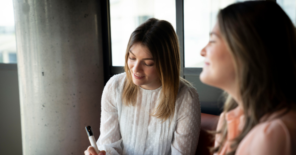 Een collega is notities aan het maken terwijl de andere kijkt en lacht